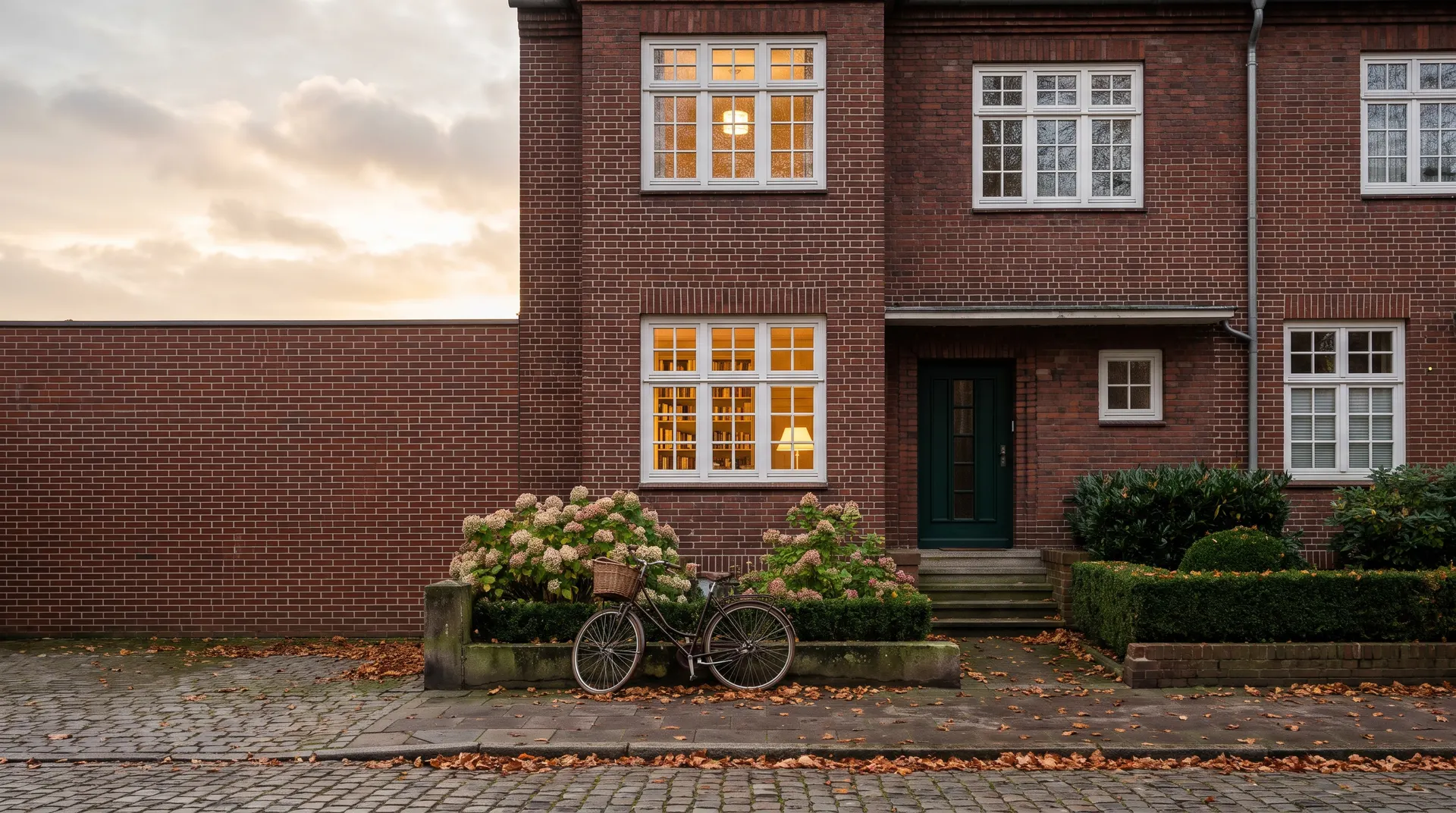 Hamburger Rotklinkerhaus im Abendlicht, Fahrrad vor dem Vorgarten, hinter den Fenstern brennt Licht